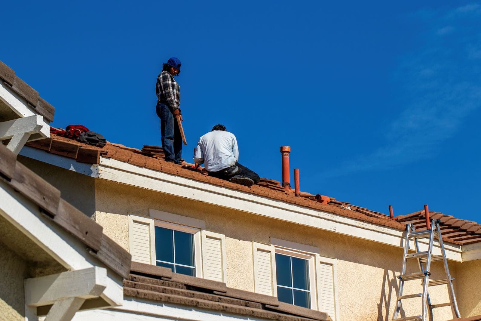 Two workers checking a house roof with a ladder at the eave