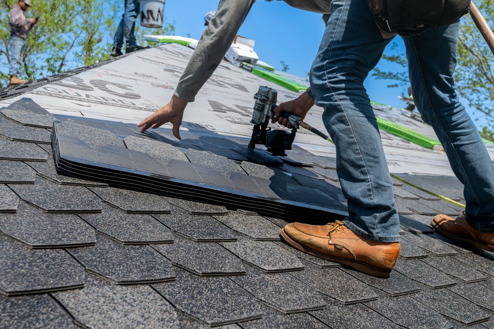 Roofer nailing new asphalt shingles with a nail gun