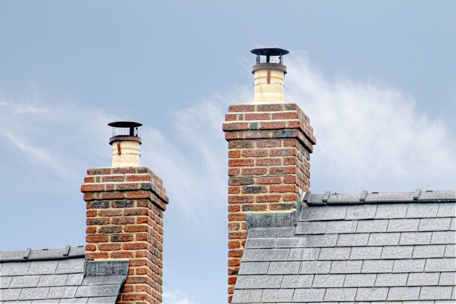 Two brick chimneys rising from a gray shingle roof
