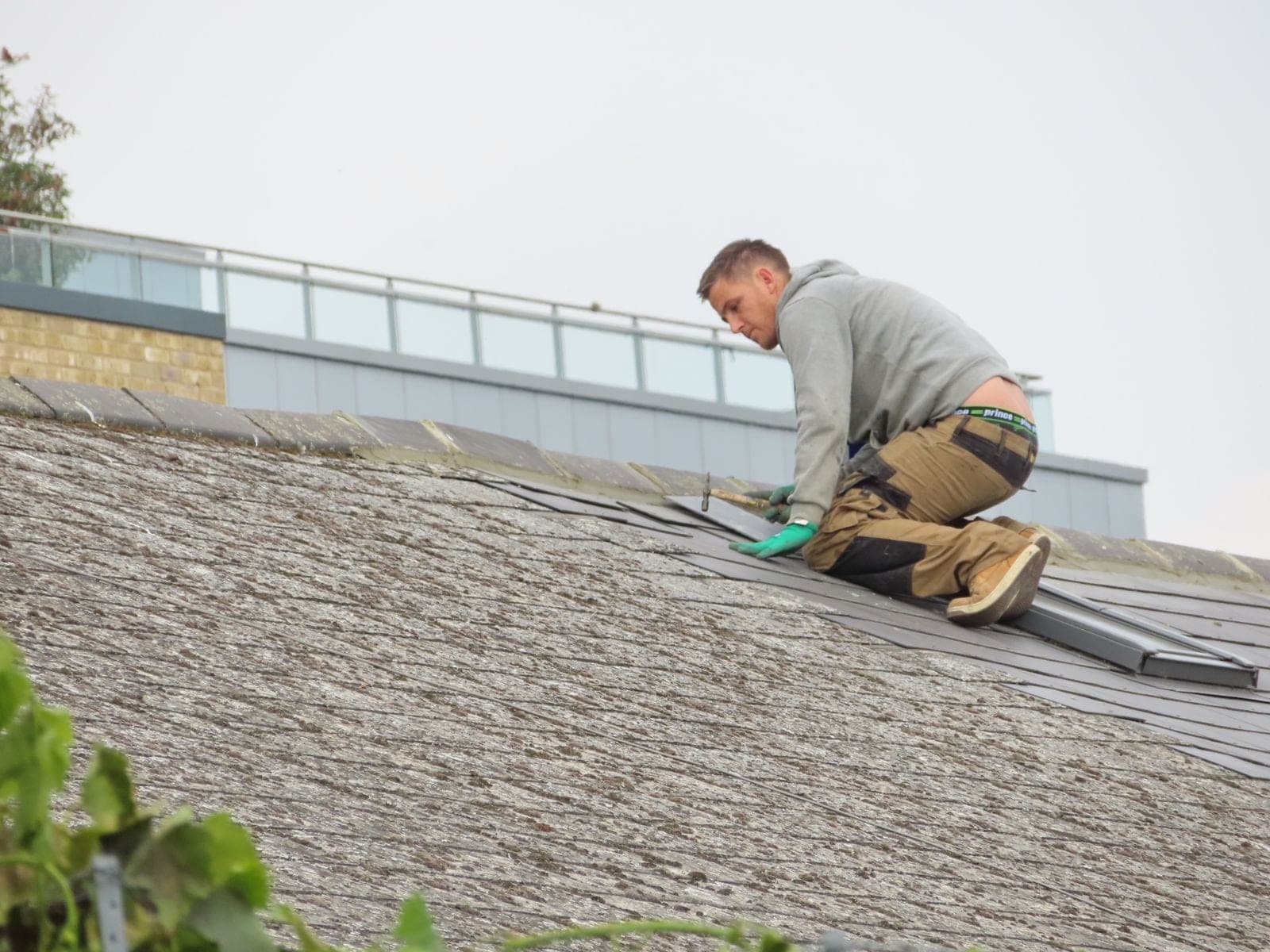 Roofer kneeling on a shingle roof doing repair work