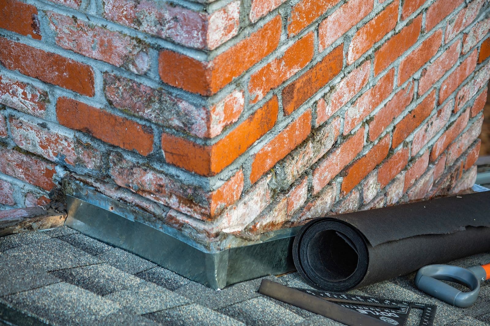 Chimney base with metal flashing and a roll of underlayment on shingles